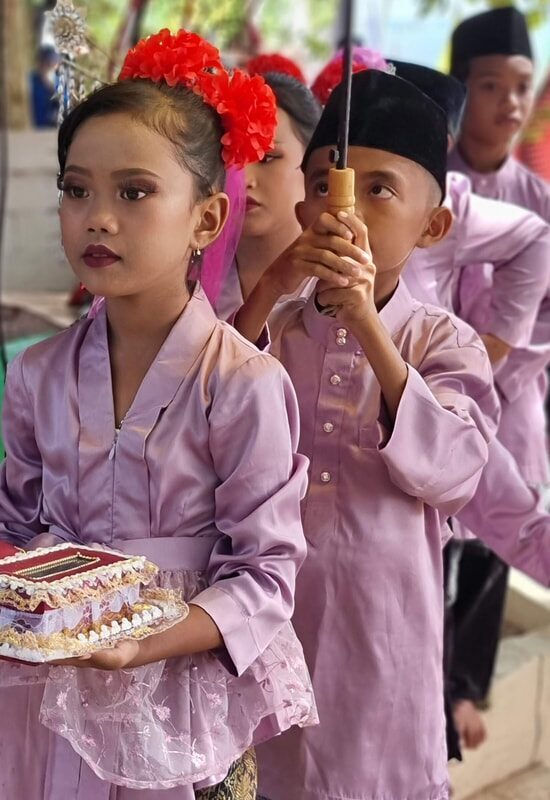 A group of girls in pink and purple traditional dress carrying an offering